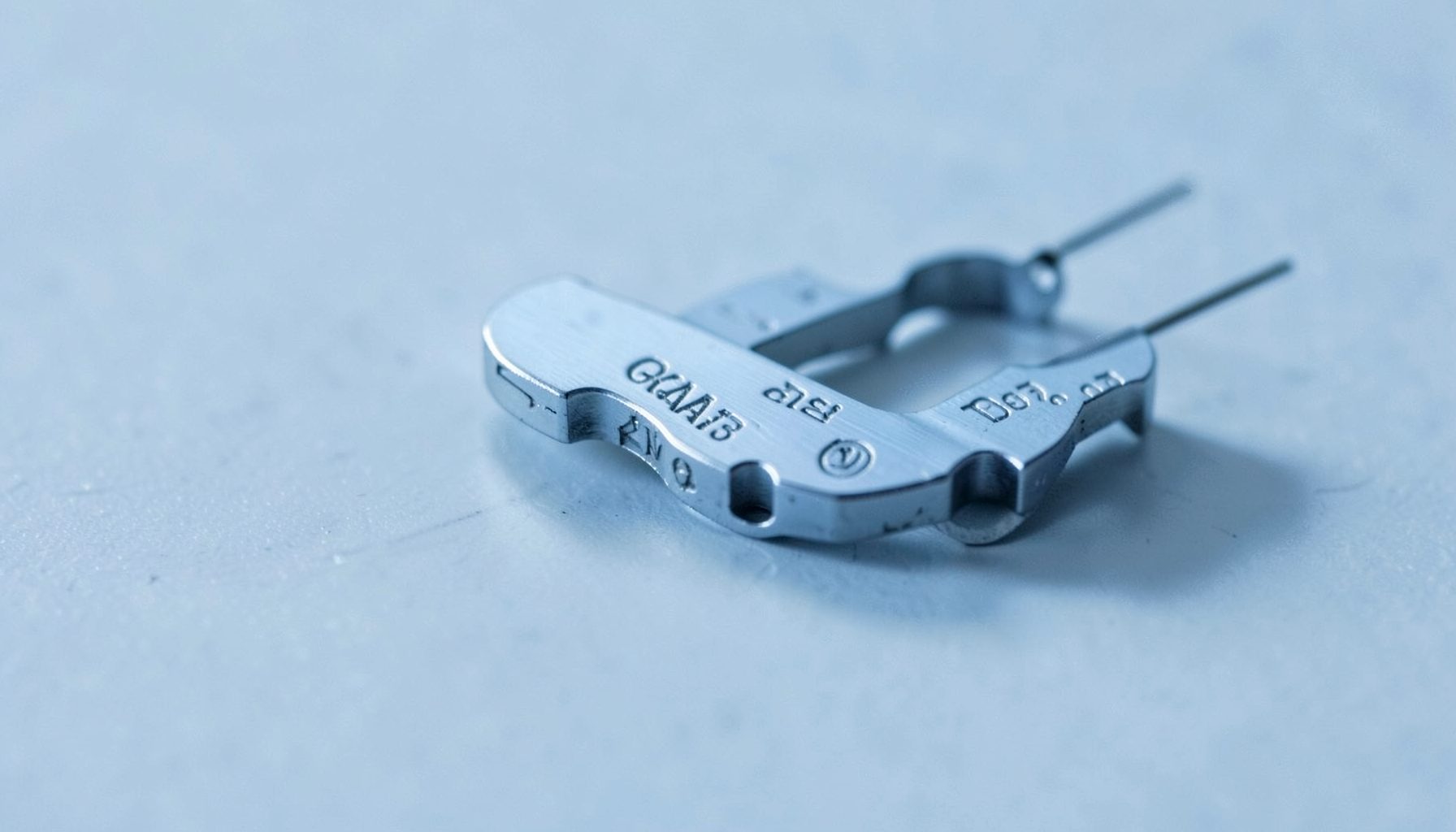 Small medical instrument components with fine engraved identification marks, cool blue-gray tones, clinical and precise mood