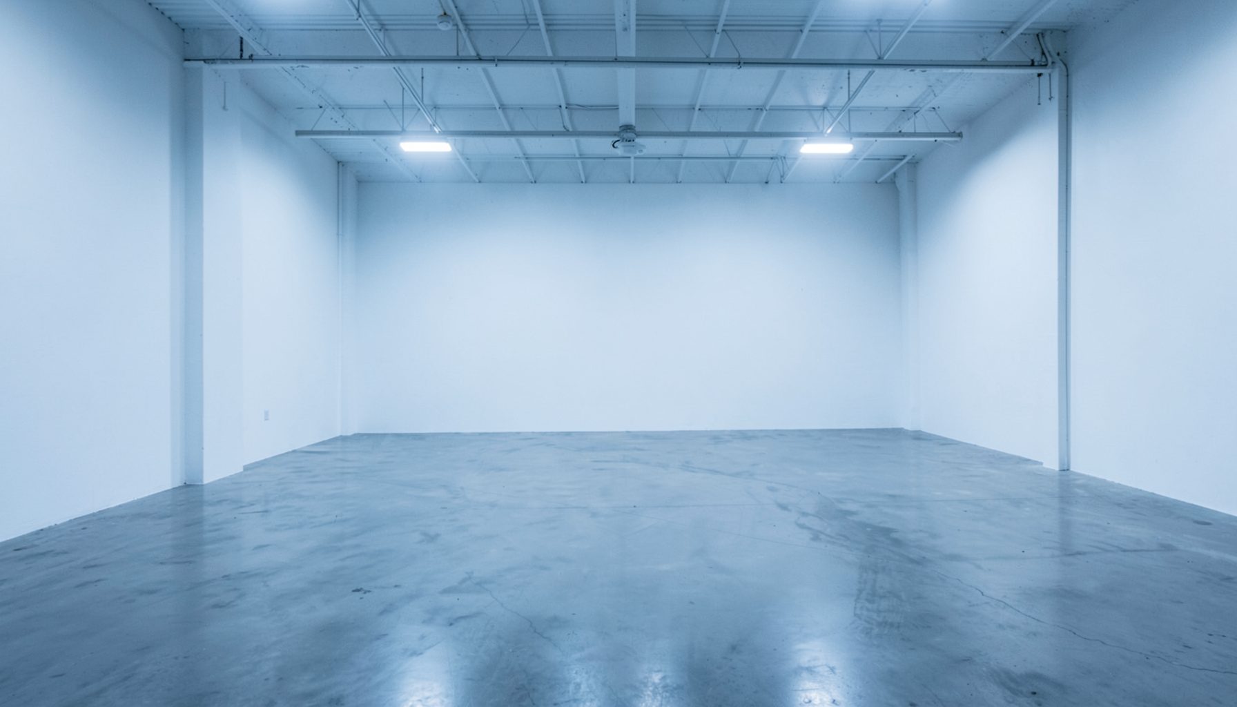 Wide industrial workshop interior with clean white walls and polished concrete floor, soft overhead lighting casting a calm blue-gray atmosphere