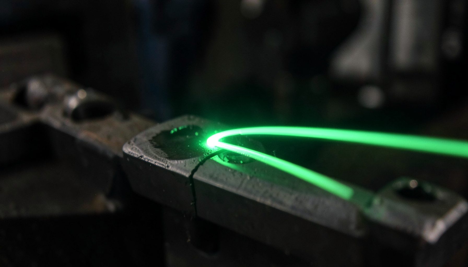 Close-up of a laser beam marking a metallic industrial component with a soft green glow, dark workshop background